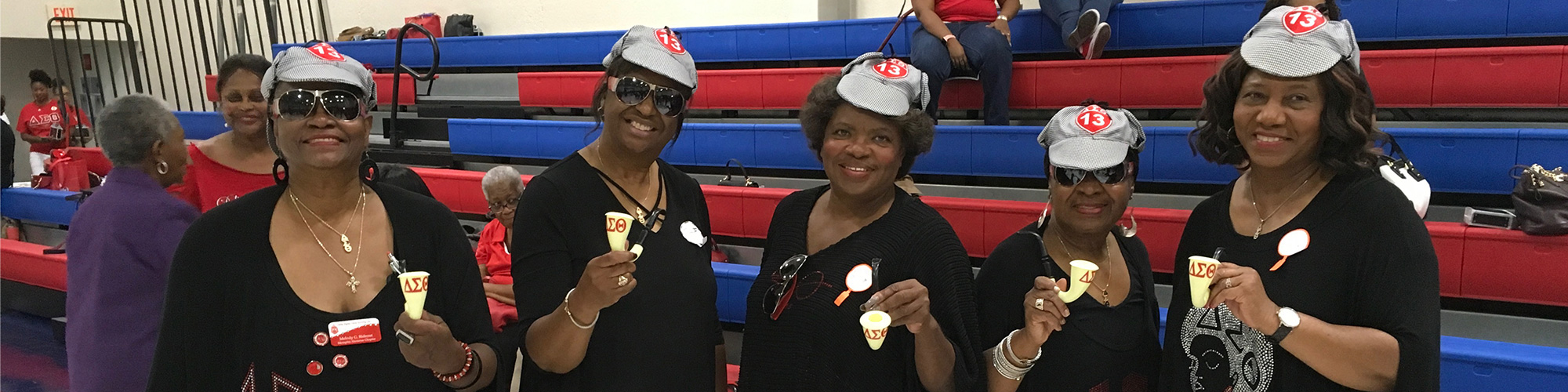 Image of five members of Delta Dears holding a pipe with the Greek letters of DST