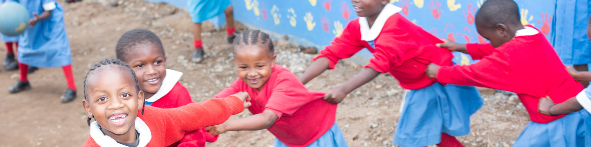 Image of five kids in single file line holding the person in front of them running and smiling. 